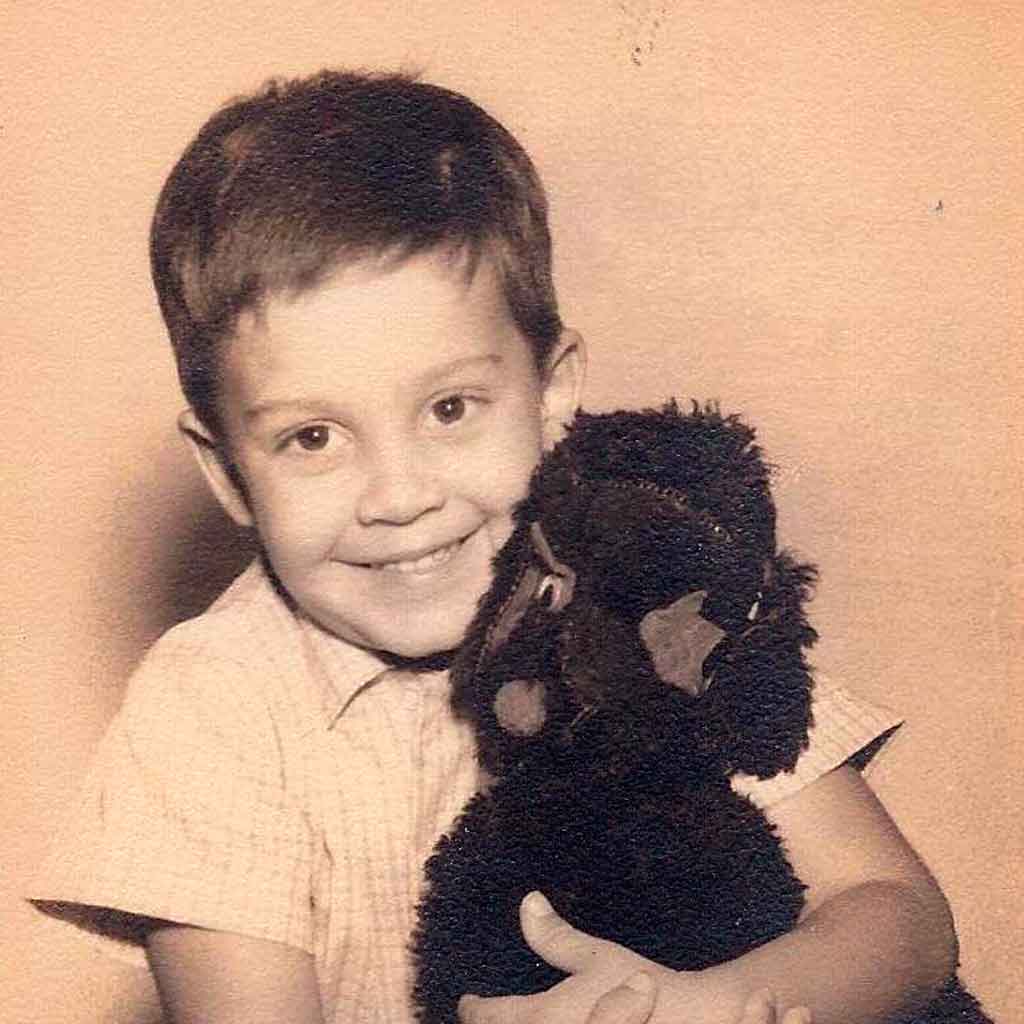 Sepia tone close up of smiling little boy hugging a beloved stuffed toy dog, which is missing an eye.