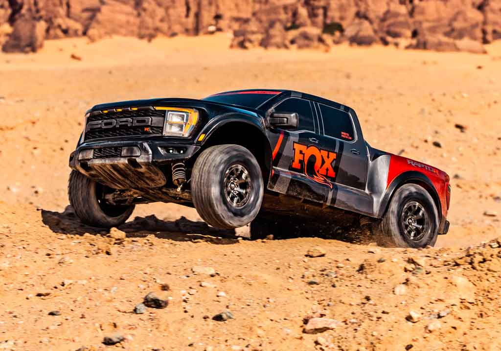 Close up of a Traxxas reduced scale model of a Ford Raptor dressed in FOX racing livery catching a bit of air on a jump.