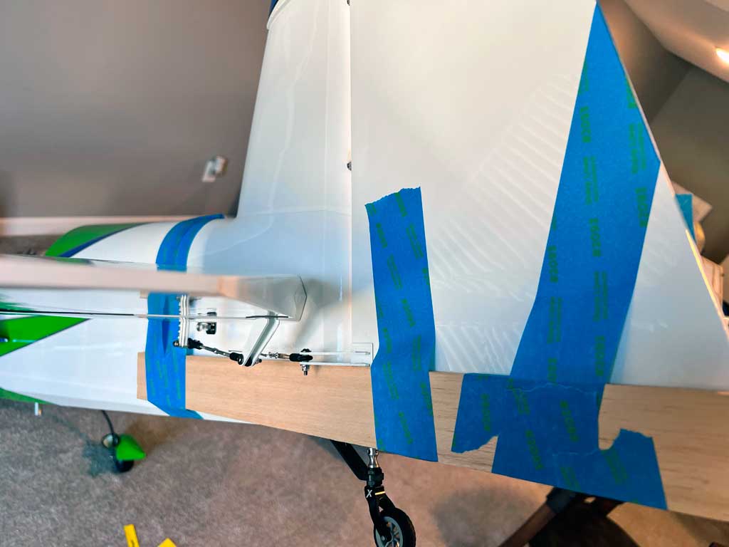 Close up showing pieces of wood held n place temporarily to secure alignment between vertical stab and rudder surface of Extreme Flight 91in Extra 300 model aircraft.