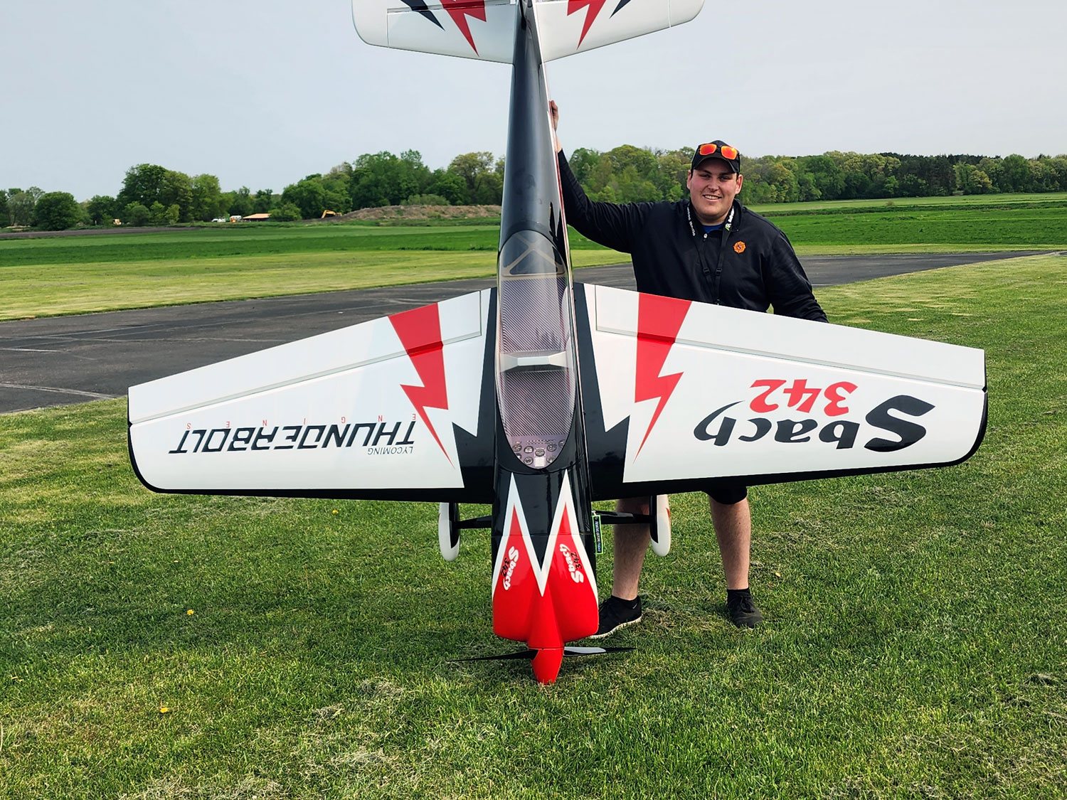 Wide angle photo of Can Devries proudly standing beside his 125 inch wingspan DLE170-powered and ProModeler servo-equipped Pilot RC Sbach 342 model
