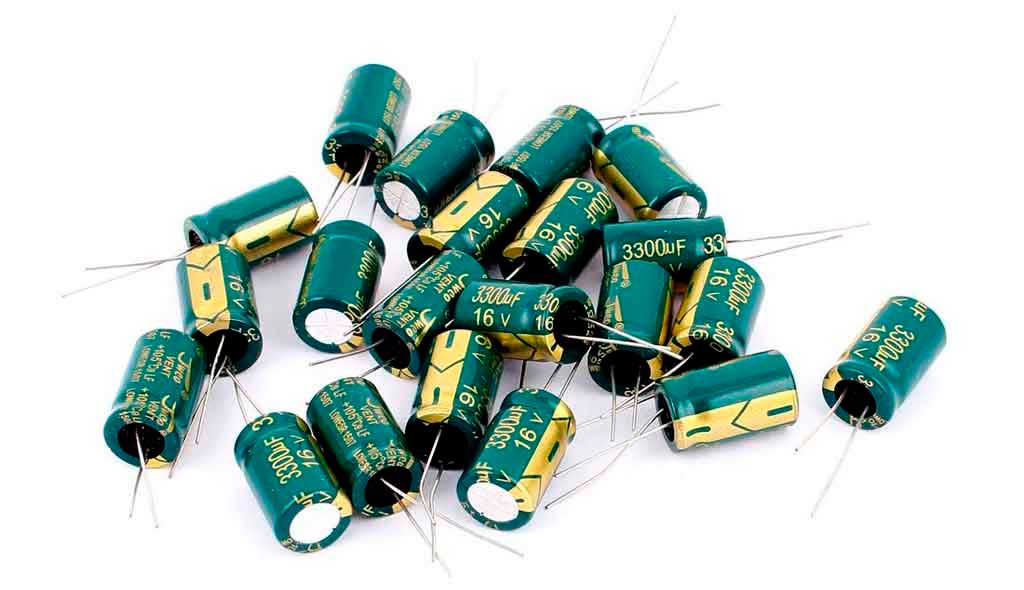 Close up of a pile of low ESR capacitors against a white background where the gold stripe marks the negative (-) leg.