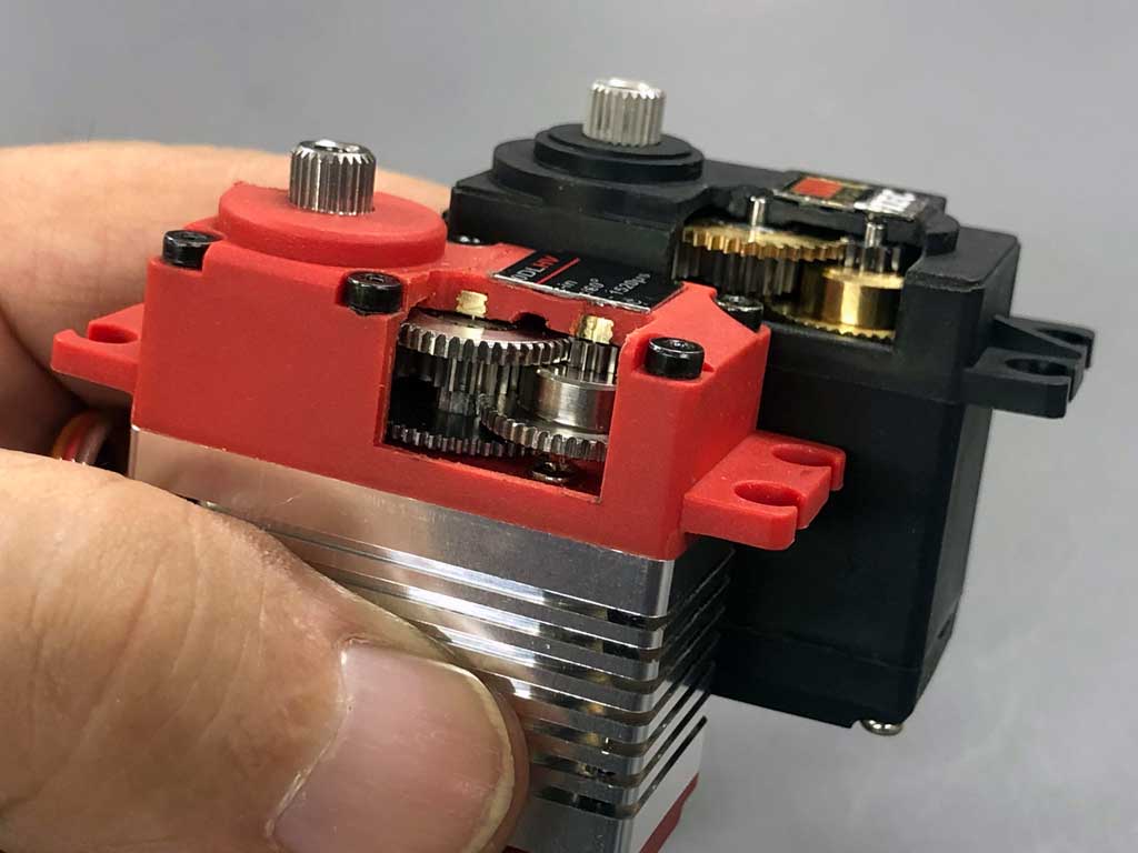 Close up a ProModeler DS180DLHV and Hitec D645MW standard class servos, both with window machined into their gear cases showing off the gear train configuration.