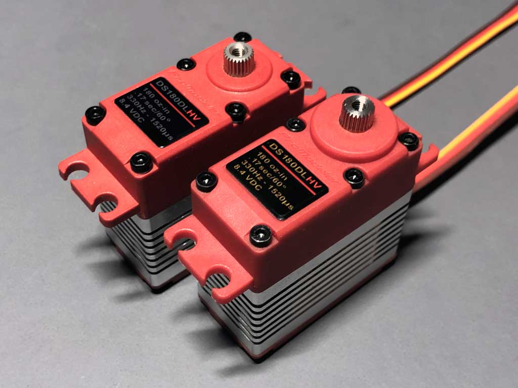 Close up of a pair of ProModeler DL-series servos side by side against a neutral gray background showcases the differences between current iteration and previous - note larger ring around output shaft strengthening the opening.
