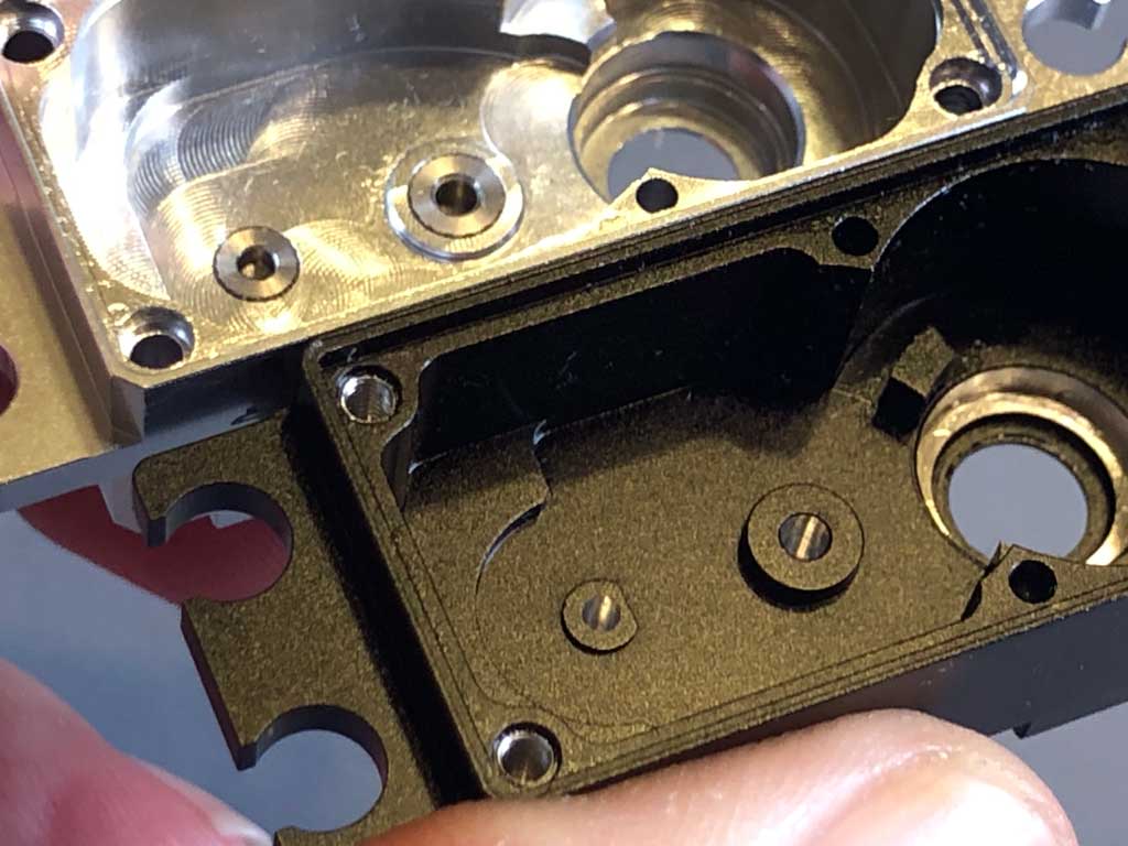 The soft gleam of the aluminum within the bore where the gear shafts are fitted contrasts against the black anodizing of the Futaba A703 upper case showcasing how Futaba hard steel gear shafts are fitted directly into soft aluminum alloy whilst the ProModeler upper has steel bushings reinforcing the aluminum for greatly enhanced durability.