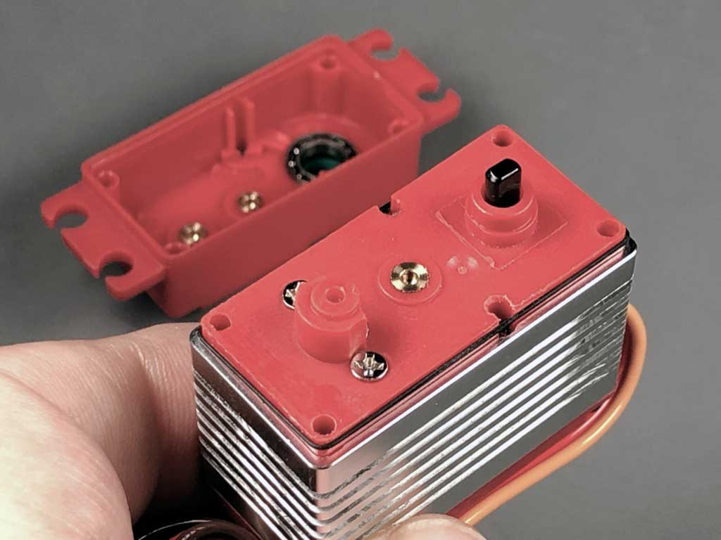 Close up of ProModeler DS180DLHV servo held in fingertips to show off the case against a neutral gray background after field stripping the gear train reveals the case reinforcements through the use of bronze bushings pressed into the polymer upper and intermediate sections.
