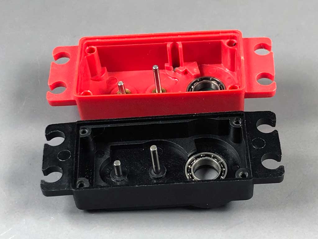 In this close up, both servos flew in the same 1/5 scale Top Flight P-51 Mustang model during the same 80 flights. Weighing in at 23 pounds and powered by a DA-85, it's a beast of an aircraft and while hard on servos, is not an atypical application. Note the subtle lean of the #2 gear shaft in all likelihood due to wear at the gear shaft pocket of the all-plastic case due to engine vibration. Meanwhile the brass bushing equipped red ProModeler servo upper case still looks brand new.