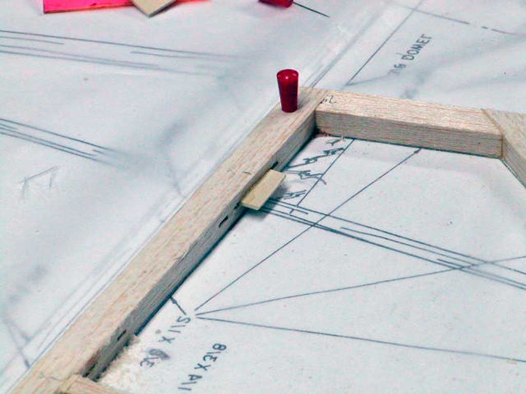Close up of balsa parts pinned to a workbench overlaying plans.
