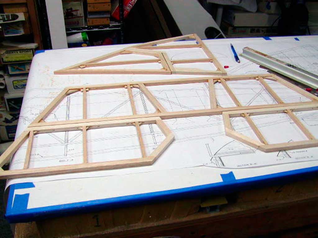 Close up of bits of balsa stock, cut to match the plans, pinned and glued to complete a model airplane's horizontal stabilizer.