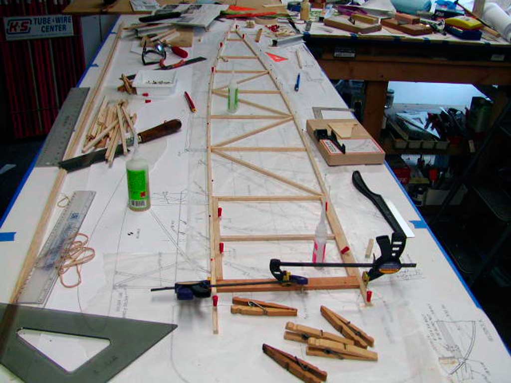 A feselage side for a WWI model of a morane-Saulnier comes togther as longerons pinned to a workbench are filled in with upright and diagonal braces.