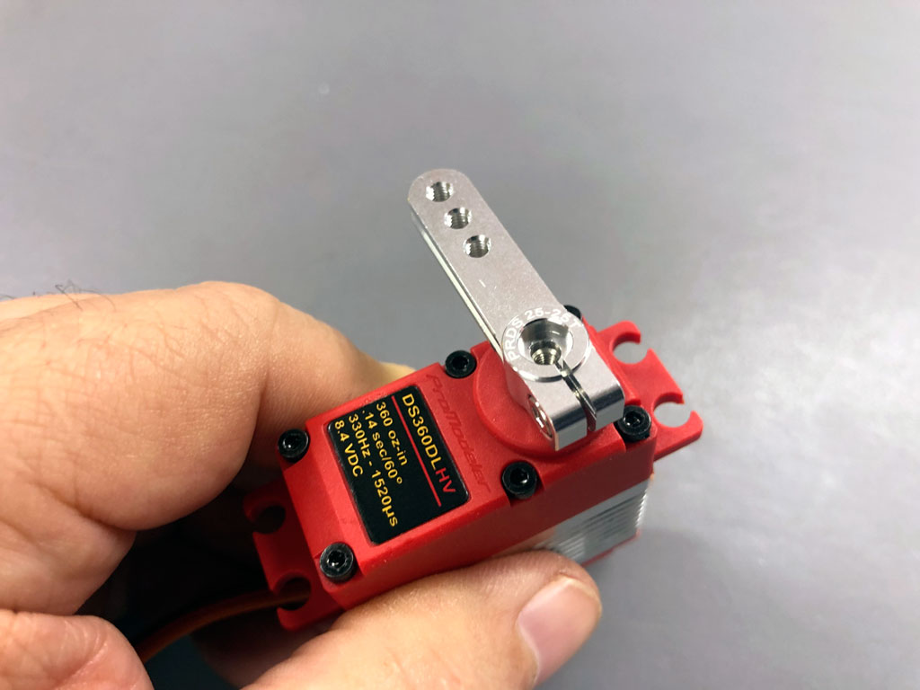 Close up of a hand against a neutral gray background holding a ProModeler DS360DLHV standard class servo equipped with PDRS25-25T alloy servo horn.