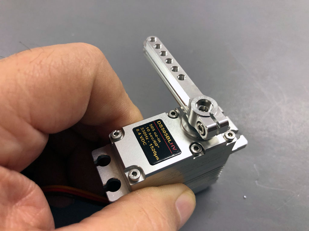 Close up of a hand against a neutral gray background holding a ProModeler DS505BLHV standard class servo equipped with PDRS40-25T alloy servo horn.