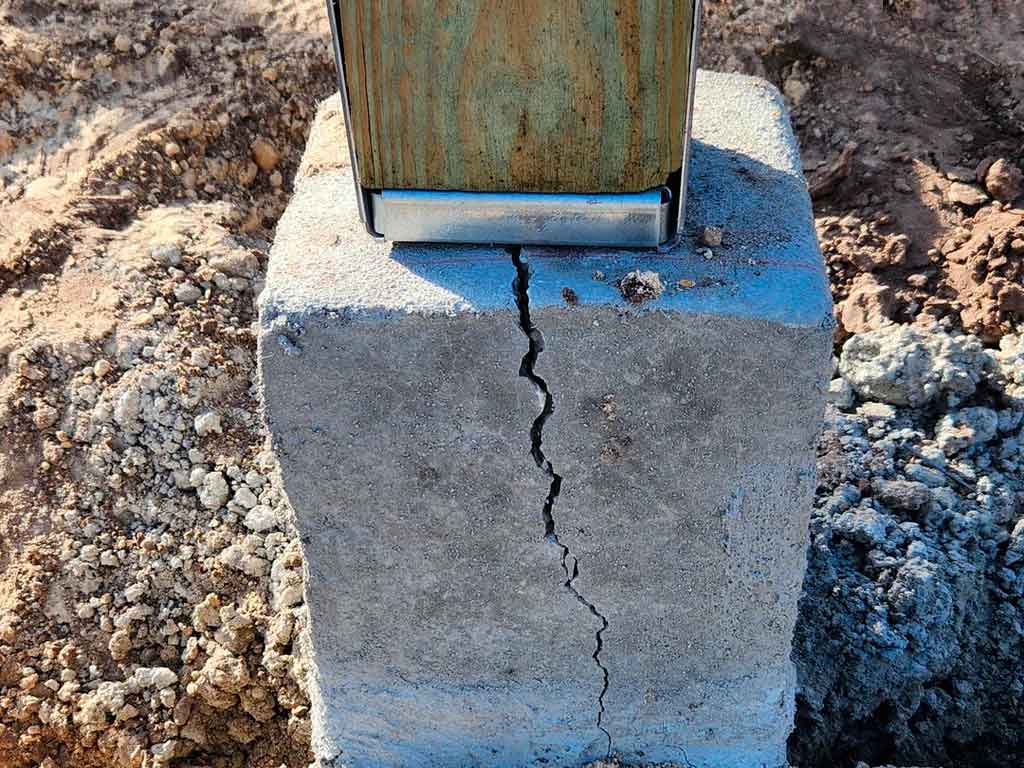 Close up photograph if a concrete foundation supporting a post which has cracked where the anchor bolt has entered the concrete, thus weaking it past recovery.