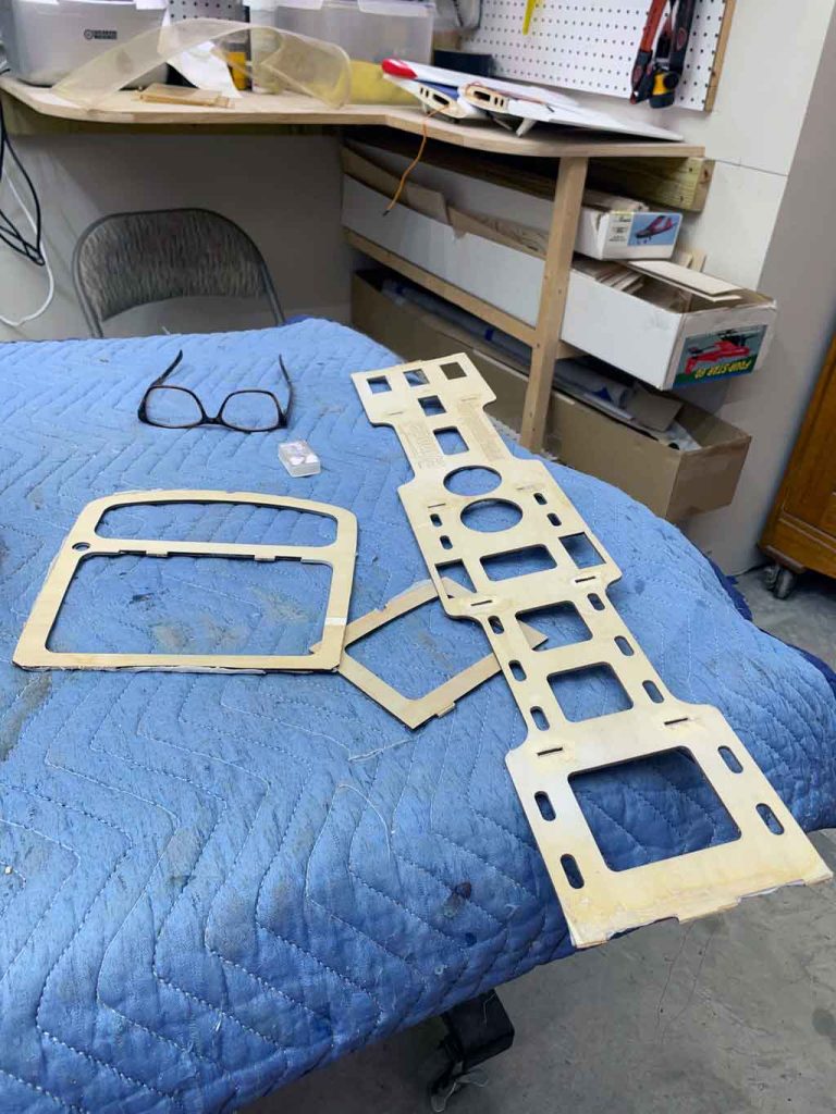 Close up of plywood model airplane parts laid out on the workbench on top of a moving blanket