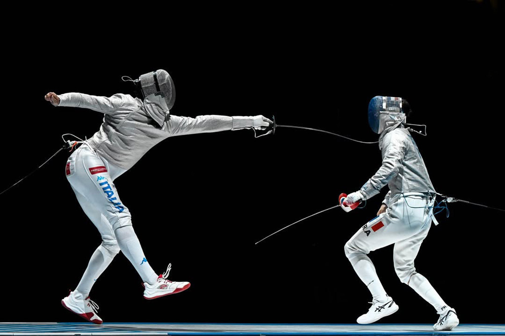 Two fencers equipped with foils, one in fleche extending his sword to the max to score the point, photo credit Azza Sports