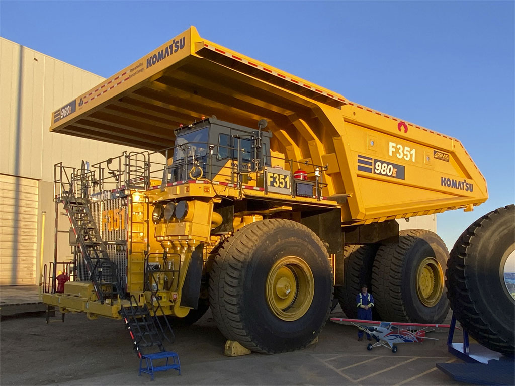 Wide angle photo of Maurice and his Hangar 9 165-inch Carbon Cub FX-3 before a giant Komatsu earth mover truck