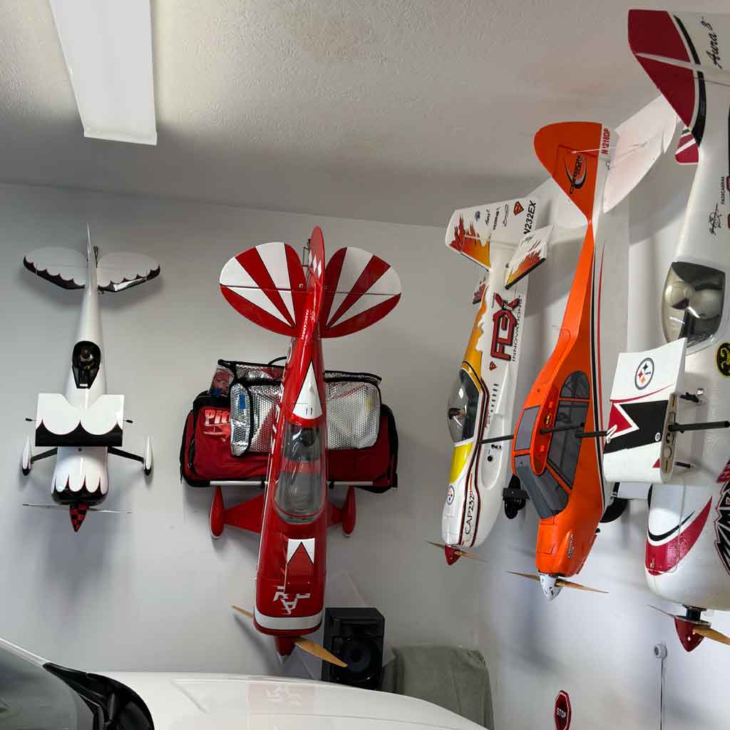 Close up of a garage wall with several model airplanes stored and hanging from their tail feathers.