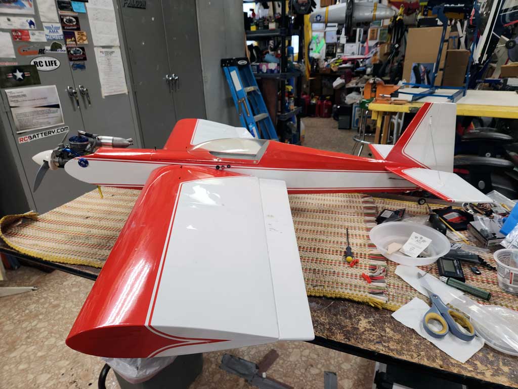Side on view of red and white SIG Somethin' Extra model airplane assembled and sitting on workbench