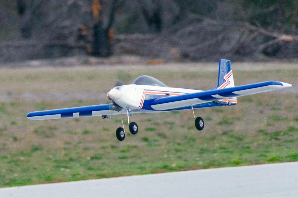 Close up of model aircraft flaring before touchdown, as the blue and white Tower Hobbies Kaos 60 is steady as a rock on final approach.