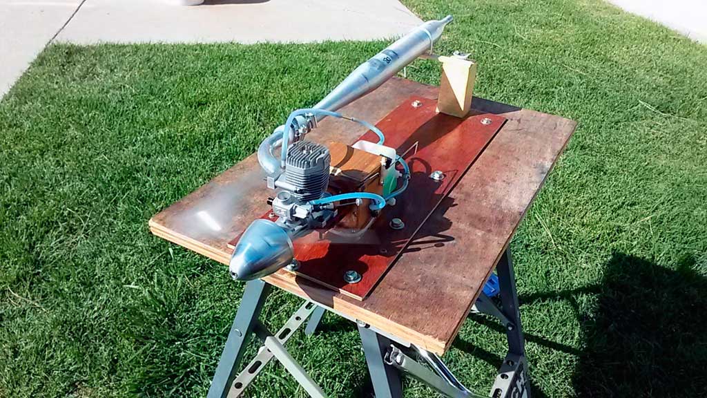 Close up of breaking in a side exhaust OS MAX 65AX with tuned pipe on the test stand before installation into a Tower Hobbies 62in Kaos.