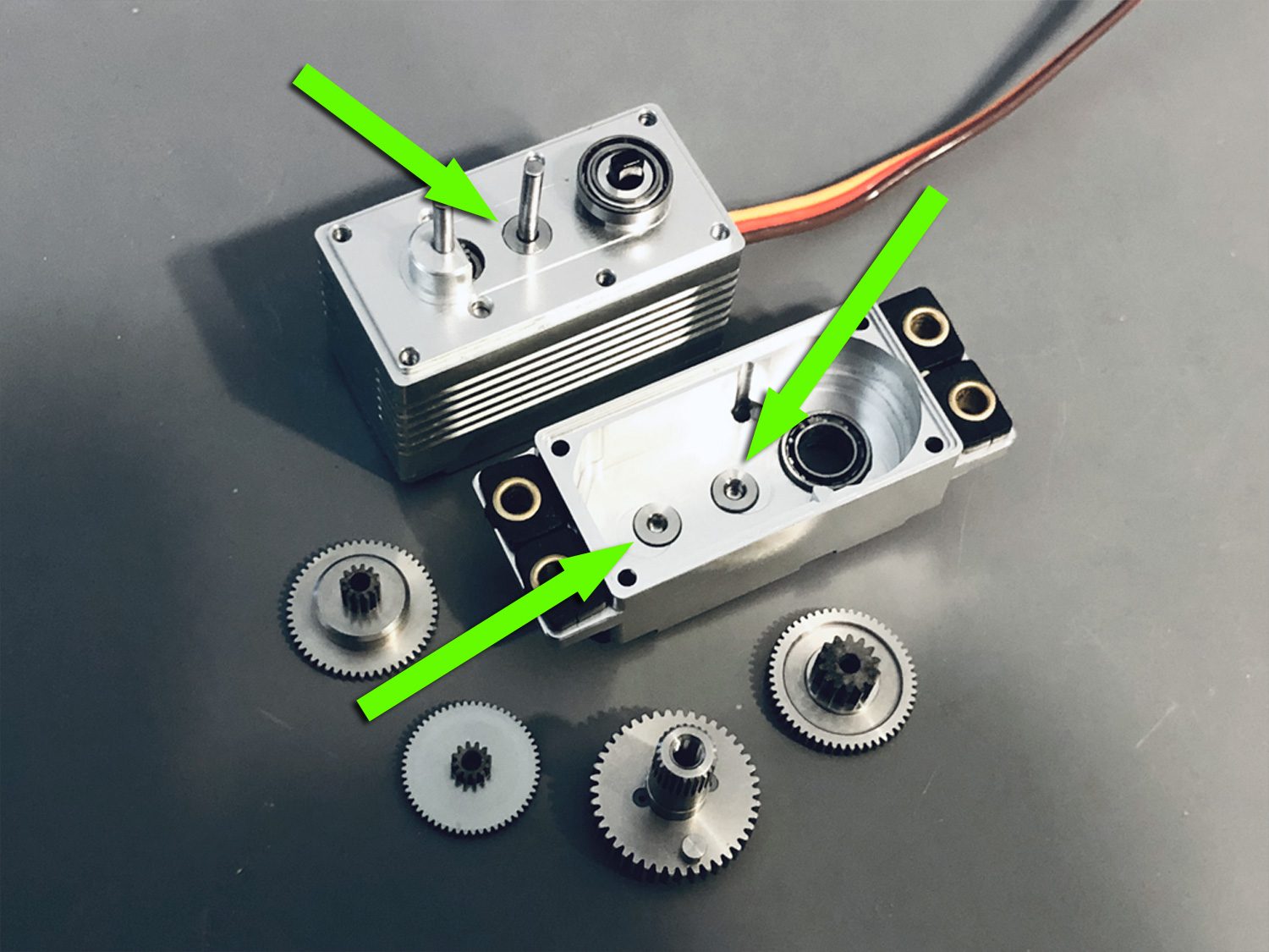 Photo of disassembled ProModeler DS505BLHV servos with three green arrows showcasing stainless steel hardpoint inserts reinforcing the 6061-T6 aircraft aluminum servo case where the stainless steel gears shafts are fitted