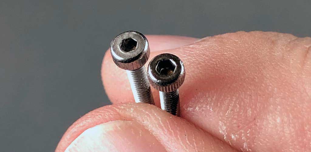 Extreme close up of M2 stainless steel Allen head bolts held within fingertips.
