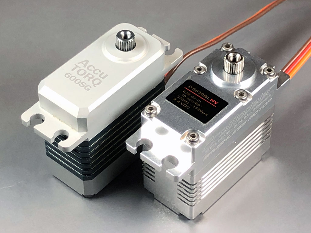 In this close up against a neutral gray background are a pair of standard-class model airplane type brushless servos, an  AccuTORQ 600SG vs ProModeler DS630BLHV.