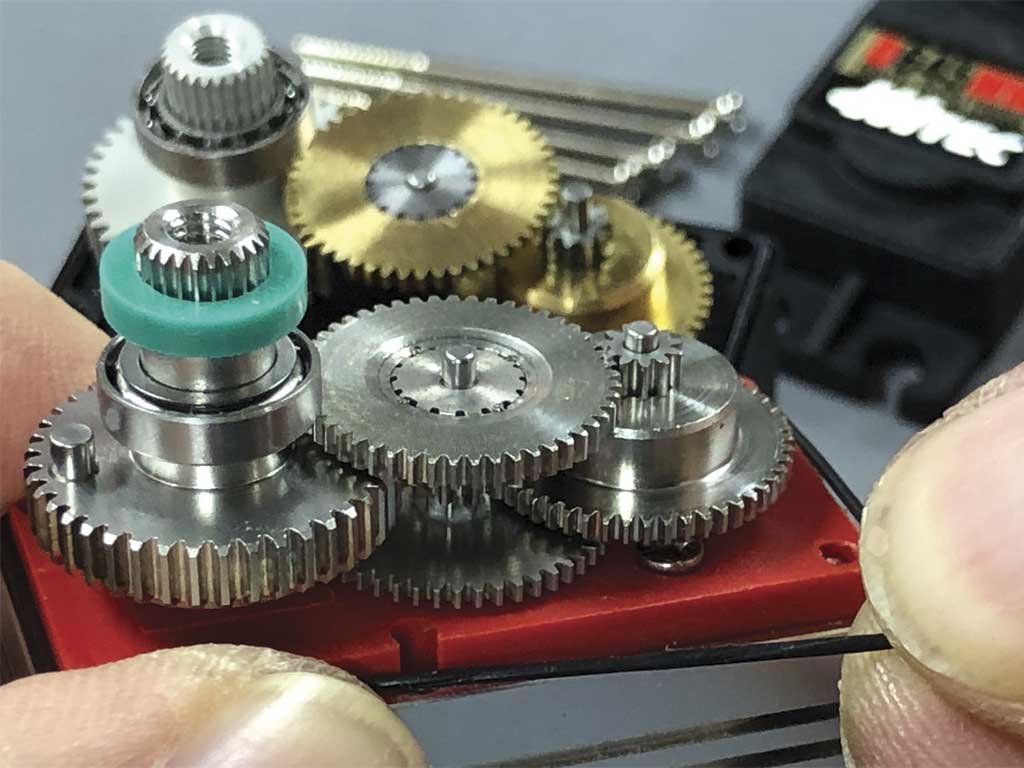 Close up photo of fingertips holding a ProModeler DS180DLHV with grear train exposed and juxtaposed against the similarly exposed gear train of a Hitec D645MW servo to showcase all-stainless gears against ordinary metal-gear standard class servos.