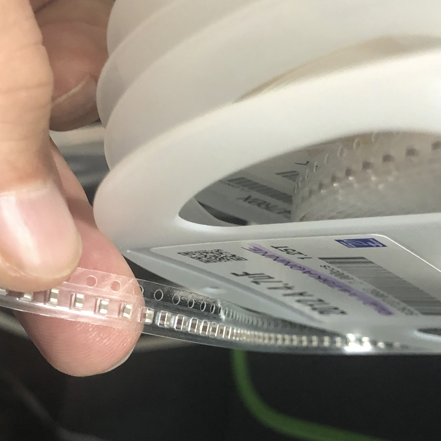 Close up of fingers holding feed stock loaded on a reel of components for a surface mount electronics pick and place machine.