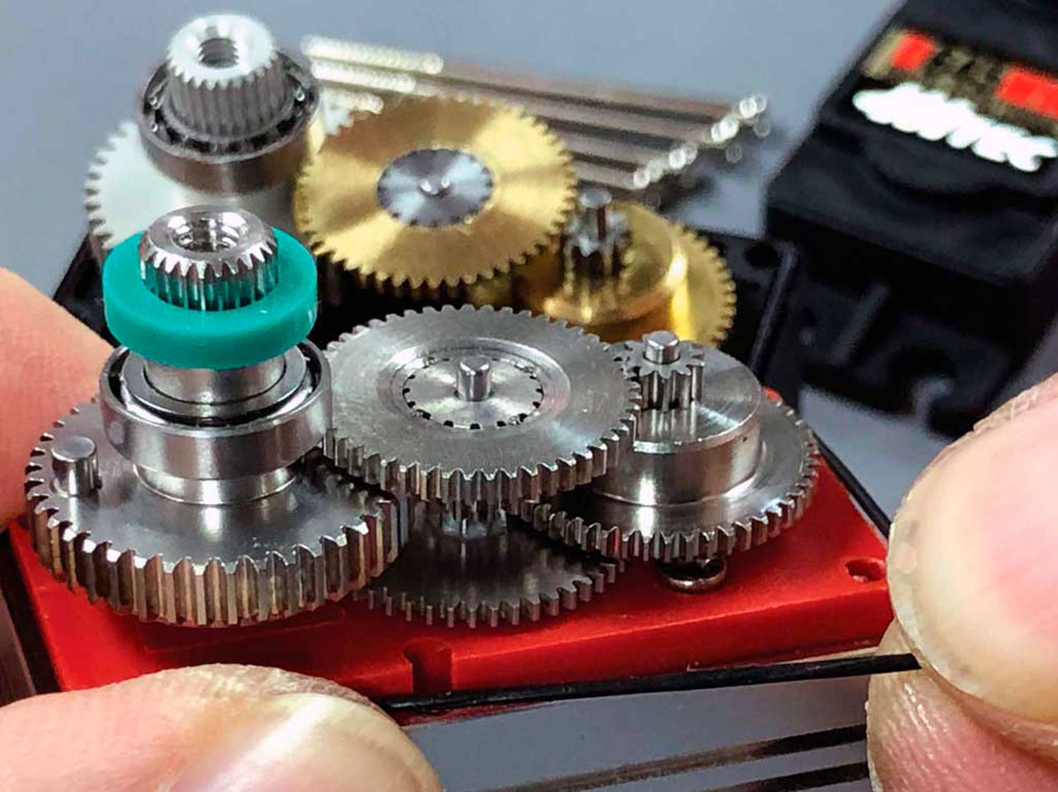 Close up photo of a ProModeler servo with gears exposed in the foreground show an o-ring being pinched between thumb and forefinger whilst in the background is a Hitec D645MW sans any o-rings for protection.
