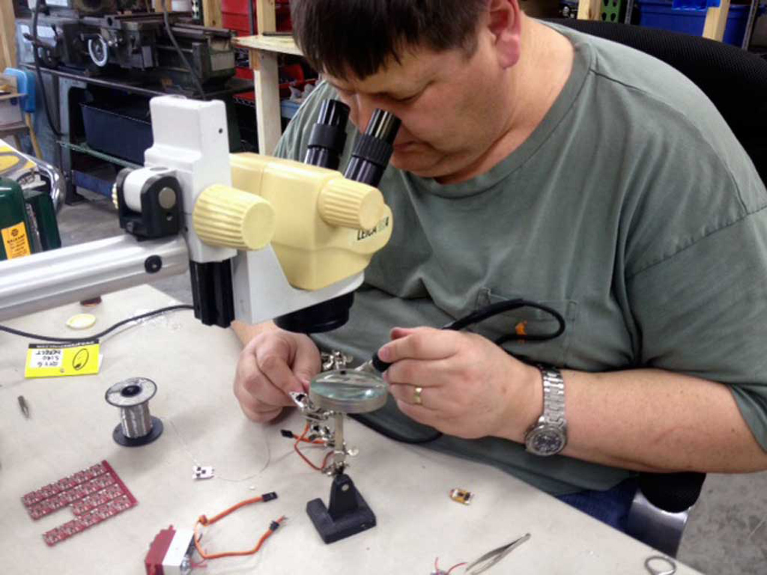 Close up of a repair in progress as a technician at a workbench, with the aid of low power microscope (Leica 3X), solders a surface mount component back in place - does require a very stead hand!